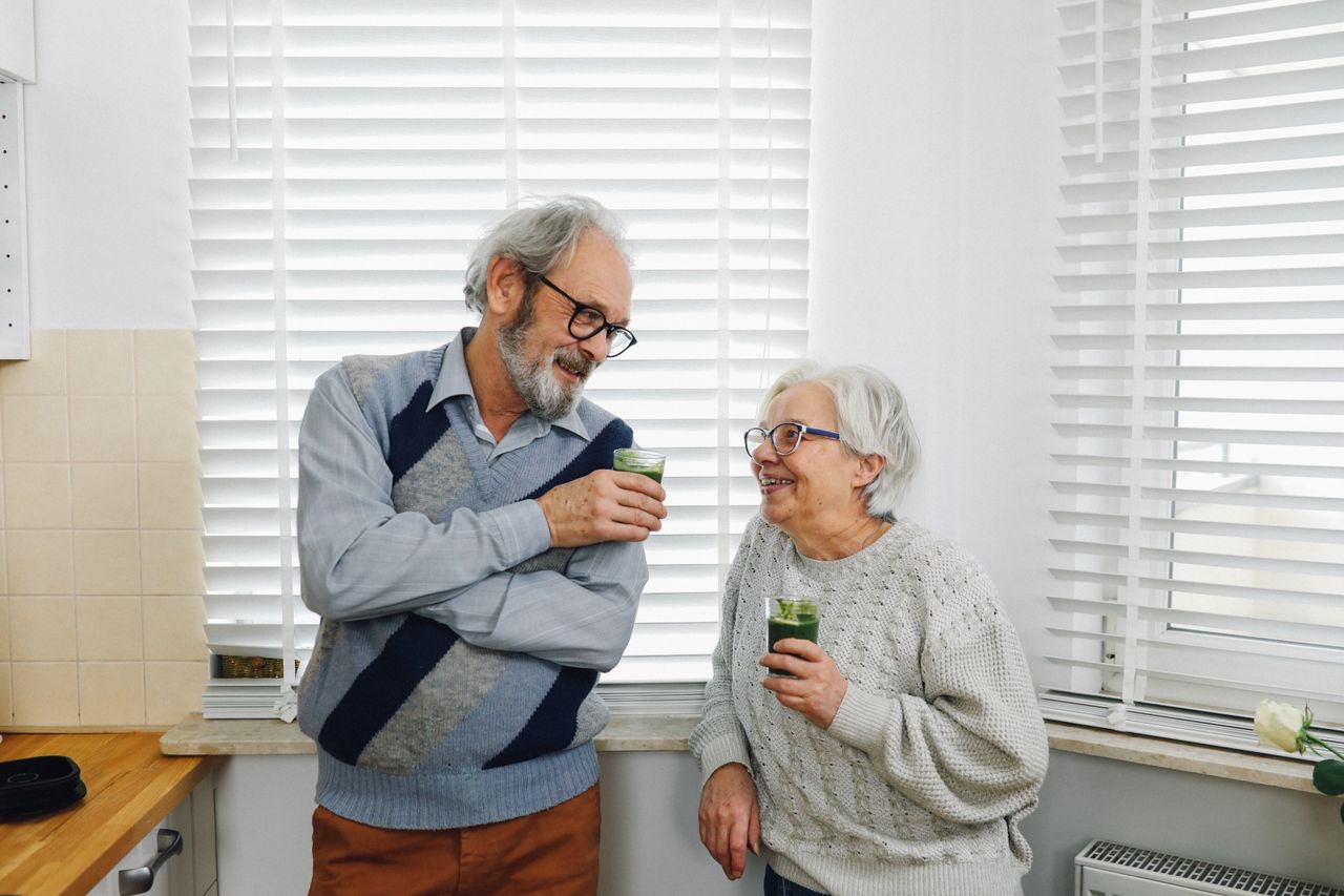 award-img Senior couple smiling and enjoying green smoothies in a cozy kitchen setting.