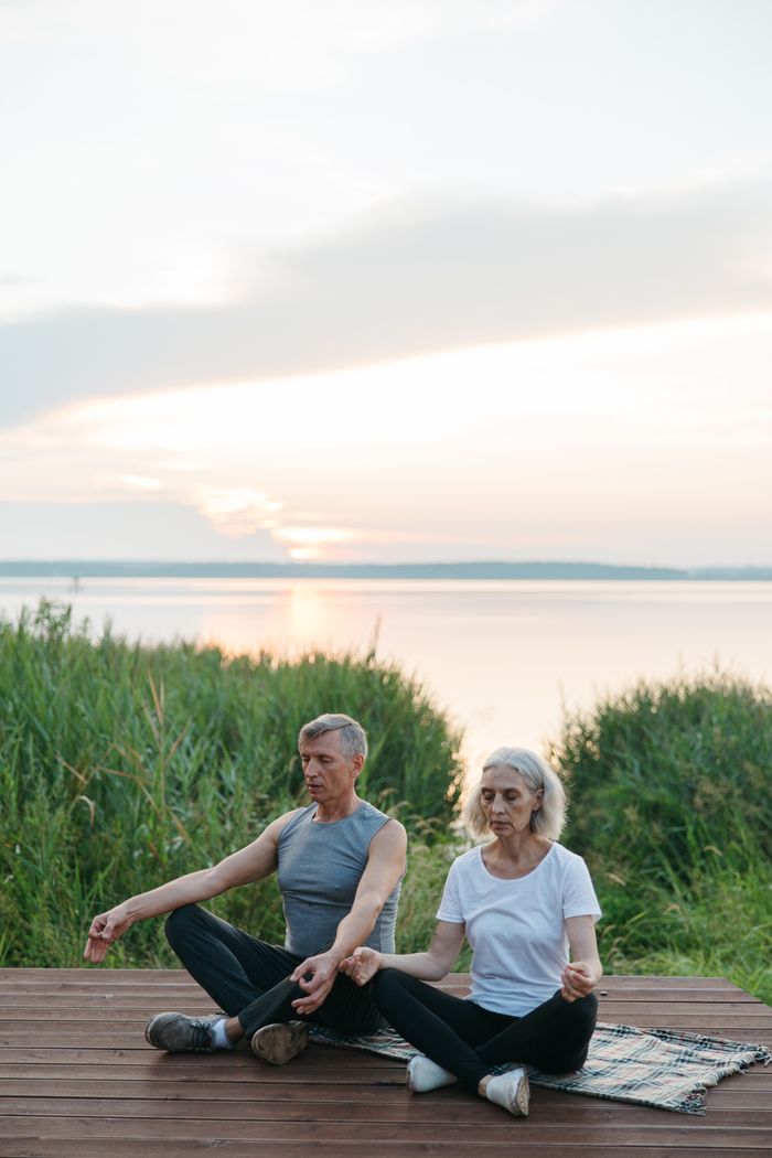 Elderly couple practicing mindfulness and meditation by the lake during sunrise.