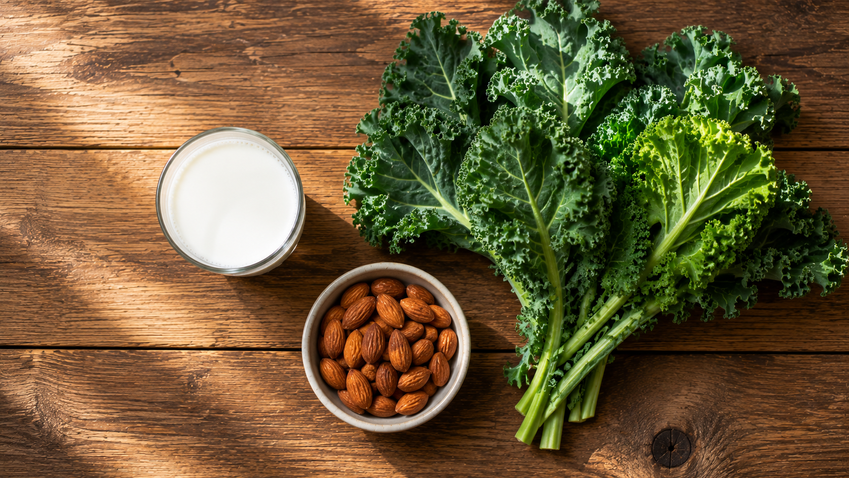 A glass of milk, almonds, and kale arranged together on a table